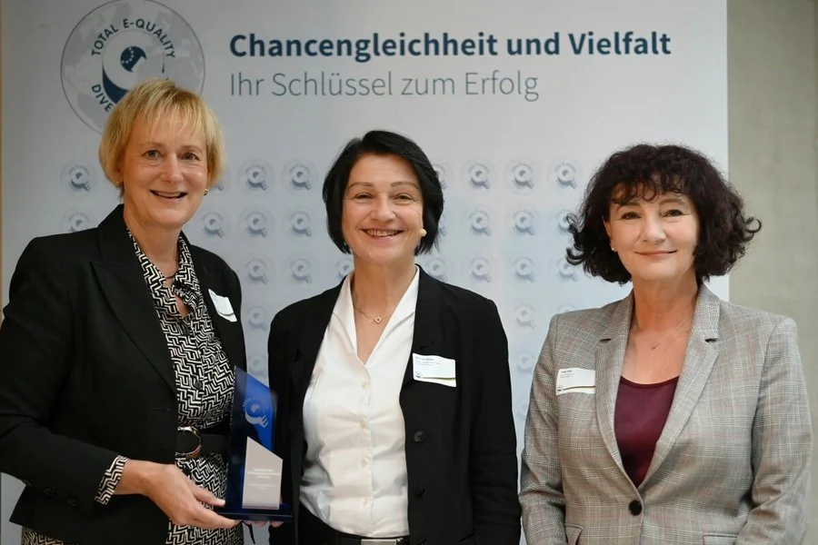 Drei Frauen stehen nebeneinander und halten stolz eine Auszeichnung in den Händen.