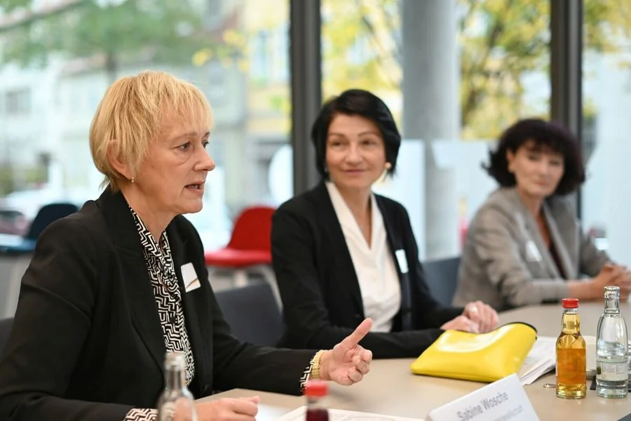 Drei Frauen sitzen an einem Tisch, umgeben von Getränken und Unterlagen und präsentieren Ergebnisse.