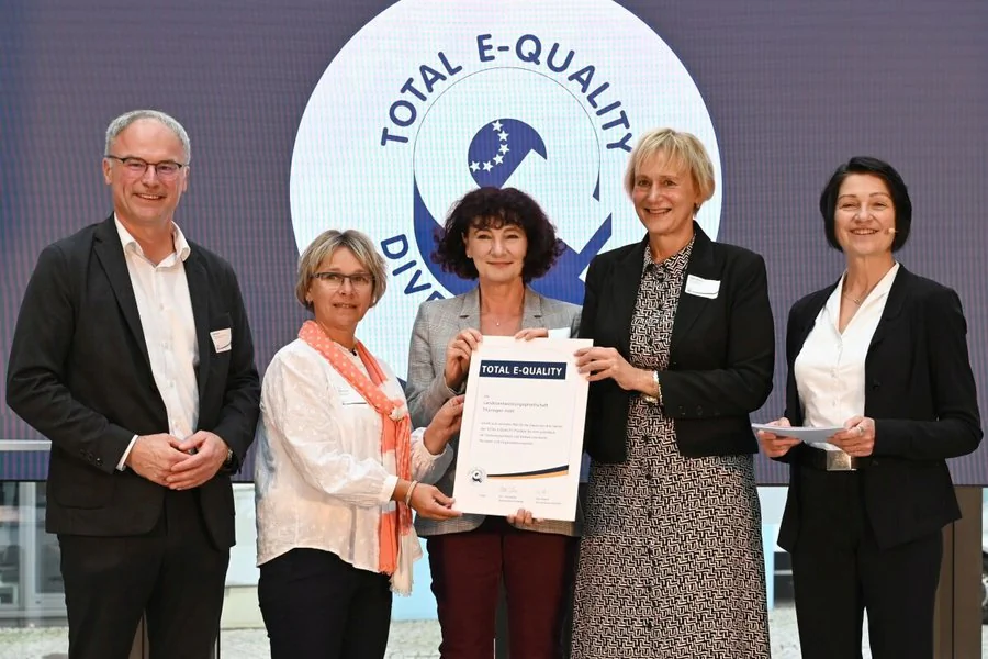 3 von 5 Personen präsentieren stolz ein Zertifikat, das ihre Errungenschaft des Total E-Quality Zertifikates.