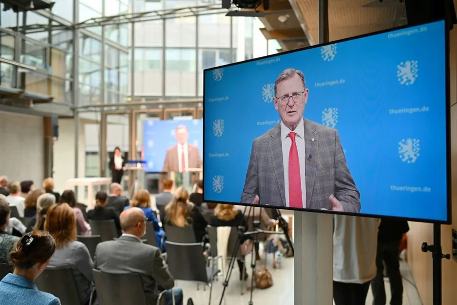 Bodo Ramelow spricht auf einem Bildschirm, während die Zuhörer aufmerksam zuhören.